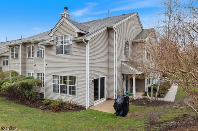 back of property with a yard, a patio, a chimney, and a shingled roof