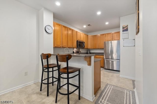kitchen featuring dark countertops, a breakfast bar area, stainless steel appliances, recessed lighting, and a peninsula