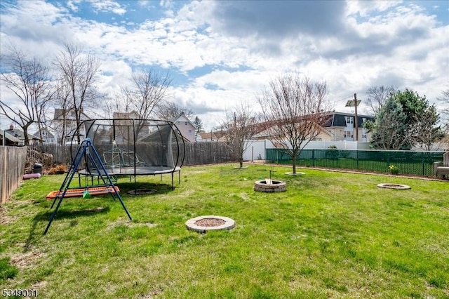 view of yard featuring a fenced backyard, a trampoline, and a fire pit