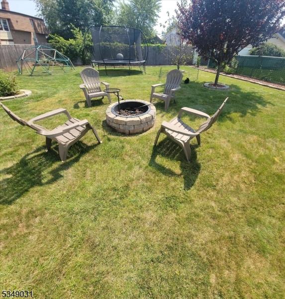 view of yard with a trampoline, fence, and a fire pit