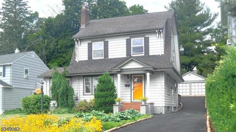 view of front of property with a chimney, a shingled roof, entry steps, an outdoor structure, and a detached garage