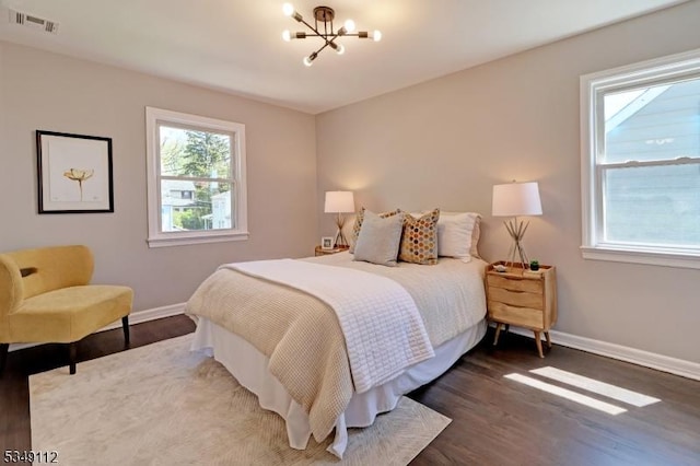bedroom with baseboards, an inviting chandelier, wood finished floors, and visible vents