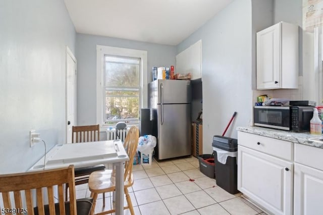kitchen with stainless steel appliances, light stone countertops, white cabinetry, and light tile patterned floors