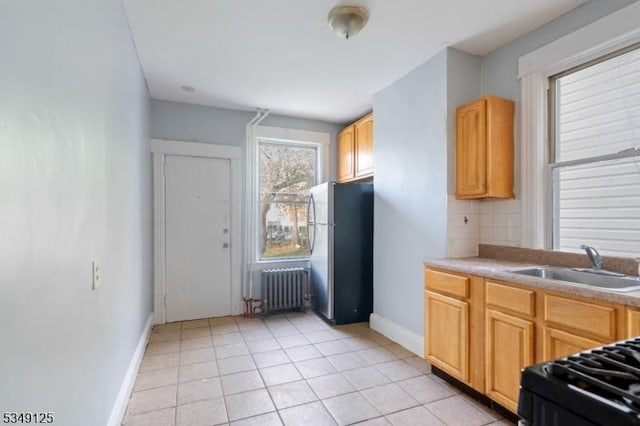 kitchen with a sink, baseboards, light tile patterned floors, freestanding refrigerator, and radiator