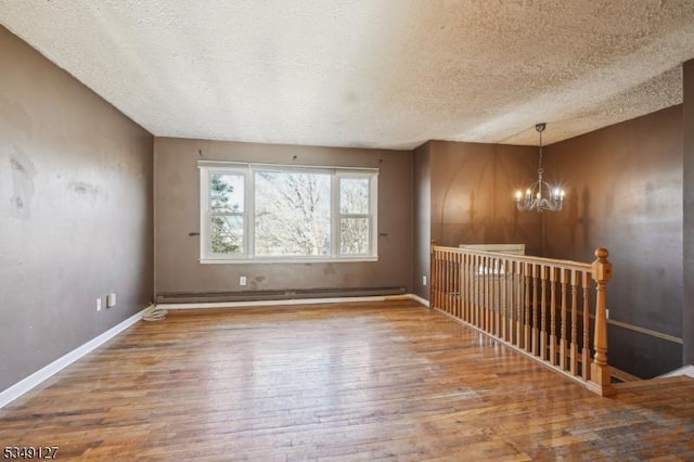 empty room featuring wood finished floors, a notable chandelier, a textured ceiling, baseboards, and a baseboard heating unit