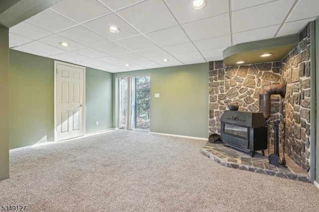 unfurnished living room with recessed lighting, carpet, baseboards, a paneled ceiling, and a wood stove