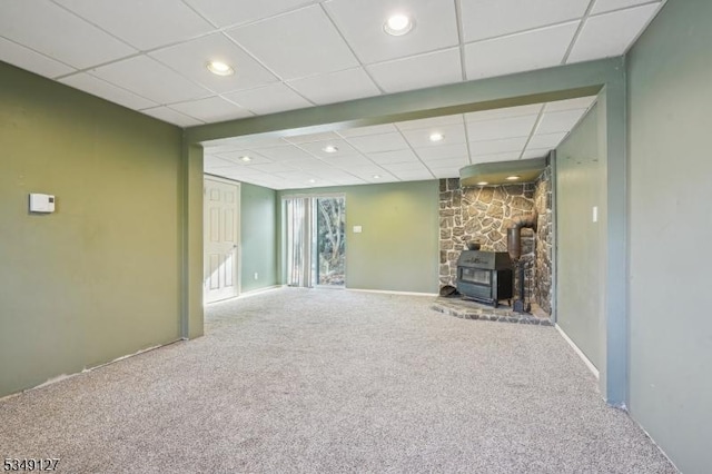 below grade area with a paneled ceiling, a wood stove, recessed lighting, and carpet