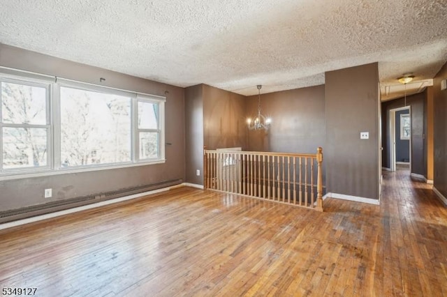 spare room featuring hardwood / wood-style floors, a notable chandelier, a textured ceiling, baseboards, and baseboard heating
