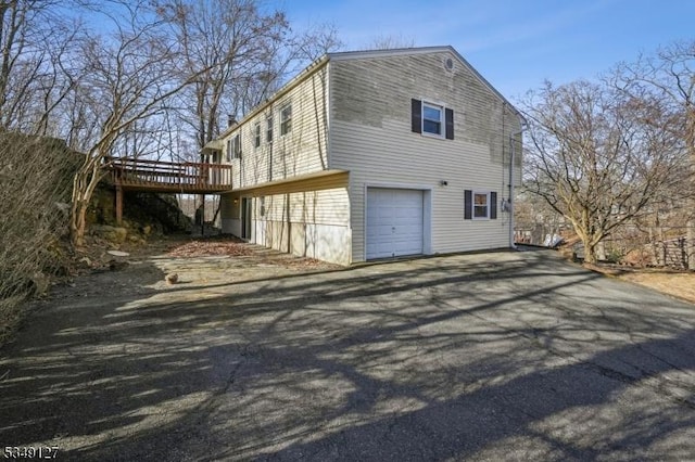 view of home's exterior featuring aphalt driveway, a wooden deck, and a garage