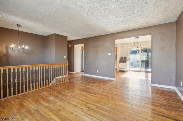 empty room featuring an inviting chandelier, a textured ceiling, wood finished floors, and baseboards
