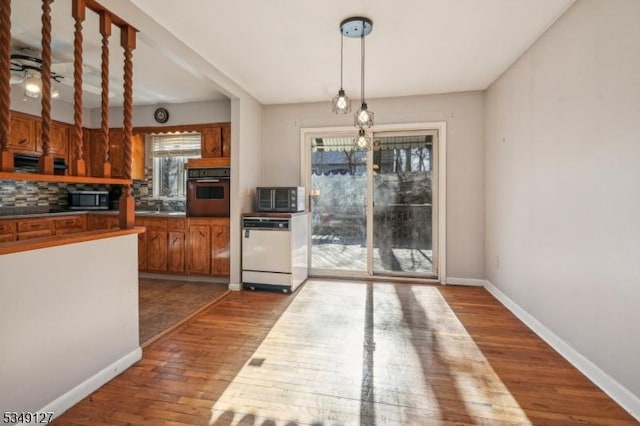 kitchen with white dishwasher, wall oven, stainless steel microwave, wood finished floors, and backsplash