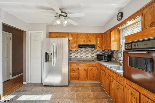 kitchen with brown cabinetry, ceiling fan, under cabinet range hood, appliances with stainless steel finishes, and tasteful backsplash