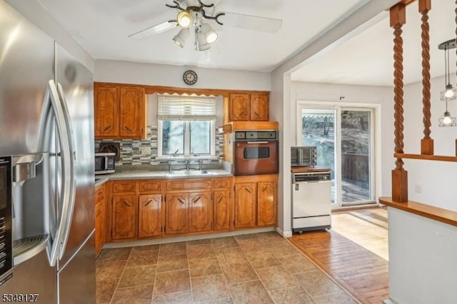 kitchen featuring ceiling fan, a sink, backsplash, brown cabinets, and stainless steel appliances