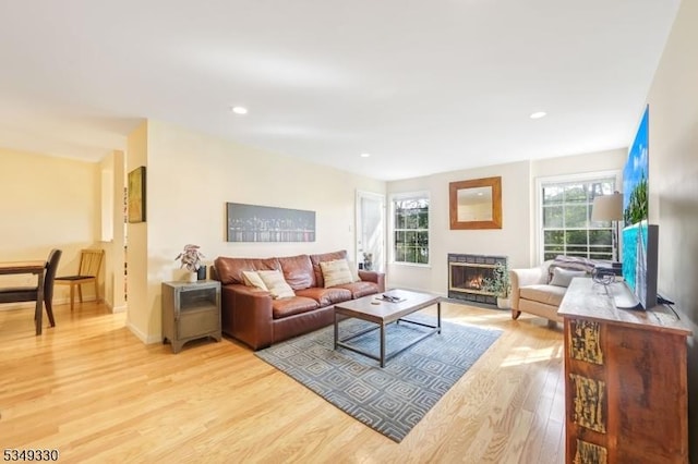 living room with a healthy amount of sunlight, recessed lighting, light wood finished floors, and a warm lit fireplace
