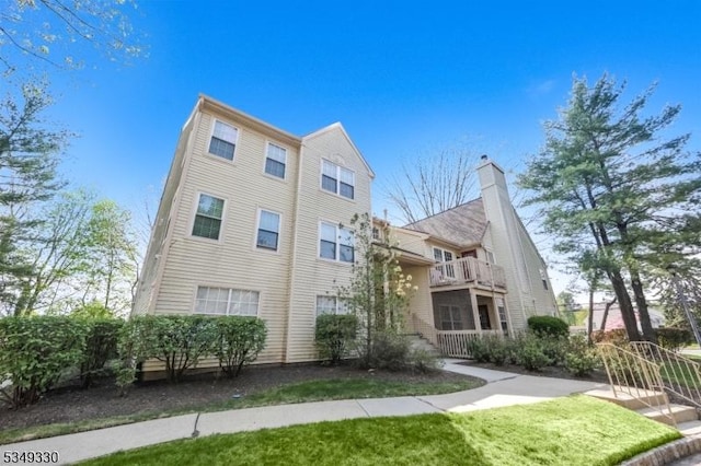 view of front facade featuring a chimney, a balcony, and a front lawn