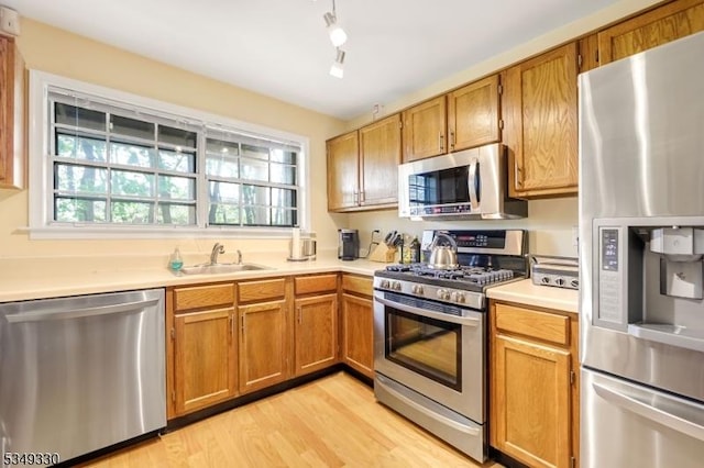 kitchen with brown cabinetry, light countertops, a sink, light wood finished floors, and stainless steel appliances