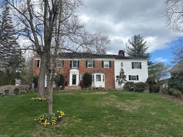 colonial-style house featuring a chimney and a front lawn