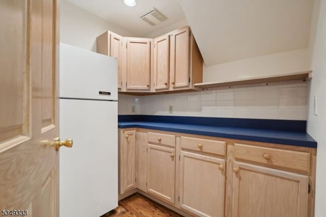 kitchen featuring freestanding refrigerator, light brown cabinets, backsplash, dark countertops, and lofted ceiling