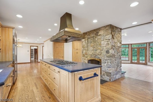 kitchen featuring island range hood, dark countertops, stainless steel gas stovetop, light brown cabinetry, and light wood-style floors
