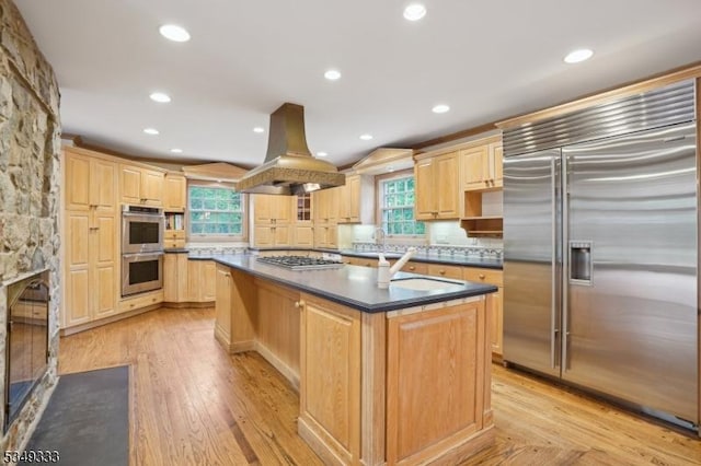 kitchen with stainless steel appliances, island exhaust hood, light brown cabinetry, dark countertops, and recessed lighting
