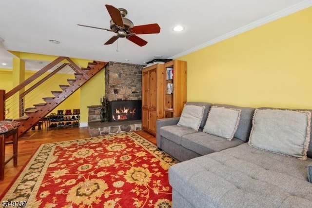 living area with a ceiling fan, crown molding, a fireplace, wood finished floors, and stairs