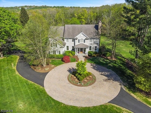 view of front facade featuring curved driveway, a front lawn, a chimney, and a forest view