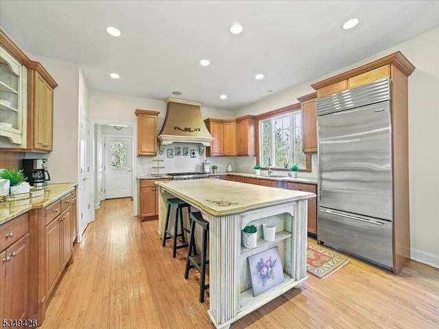 kitchen featuring light wood-style floors, a kitchen breakfast bar, custom range hood, a kitchen island, and built in refrigerator