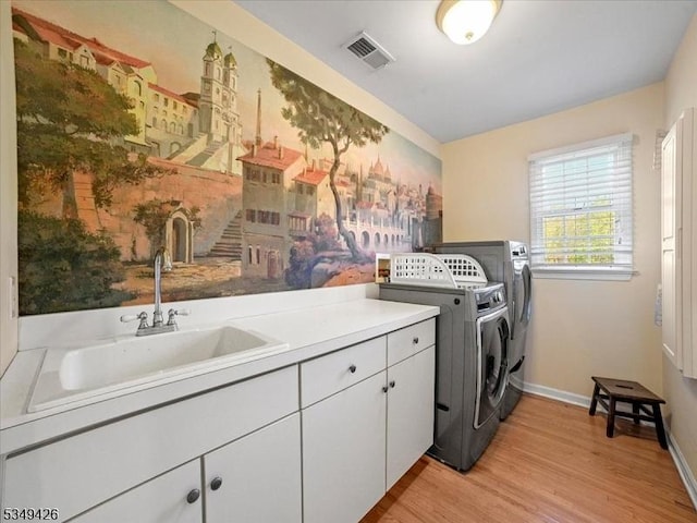 laundry area with independent washer and dryer, cabinet space, a sink, light wood finished floors, and visible vents