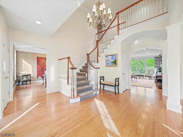 foyer featuring a towering ceiling, arched walkways, baseboards, light wood-style floors, and stairs