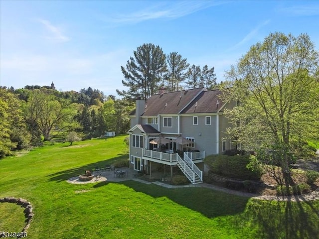 back of property featuring a chimney, a deck, a patio area, an outdoor fire pit, and a yard