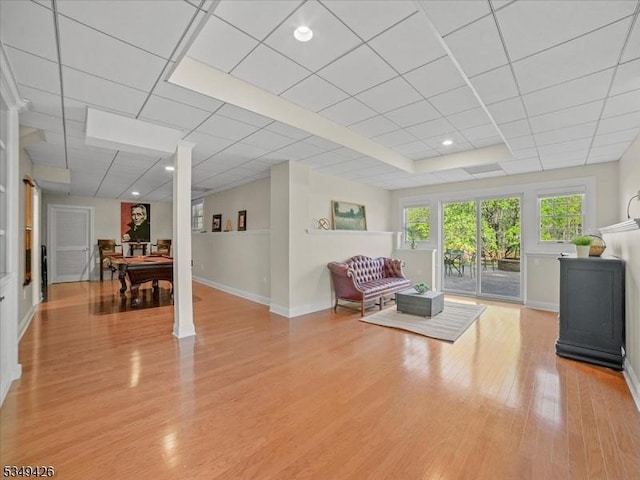 living area with baseboards, a drop ceiling, and light wood-style flooring