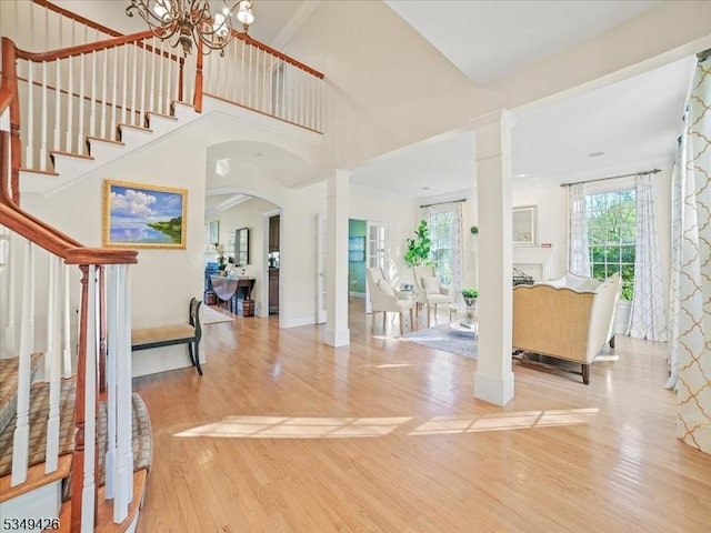 foyer with an inviting chandelier, stairs, decorative columns, wood finished floors, and arched walkways