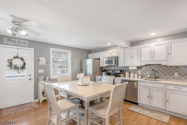 kitchen with tasteful backsplash, light countertops, stainless steel appliances, light wood finished floors, and a sink