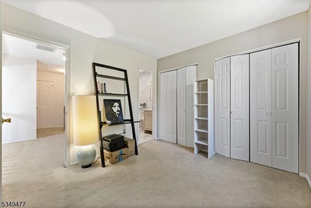 unfurnished bedroom featuring carpet flooring, visible vents, ensuite bath, and two closets