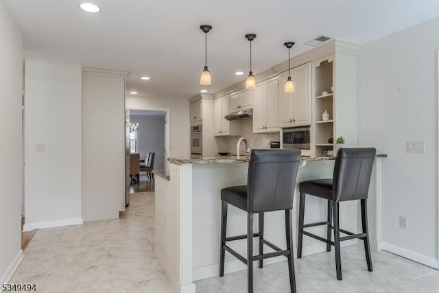 kitchen featuring stainless steel appliances, under cabinet range hood, visible vents, a peninsula, and a kitchen breakfast bar