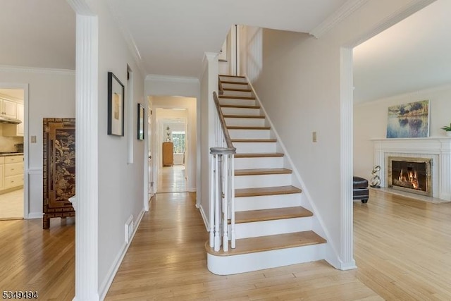 stairway with a glass covered fireplace, visible vents, baseboards, ornamental molding, and wood finished floors