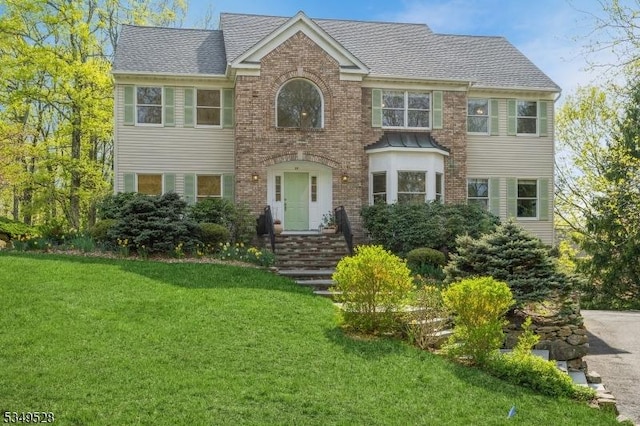 colonial-style house with a front lawn, brick siding, and a shingled roof