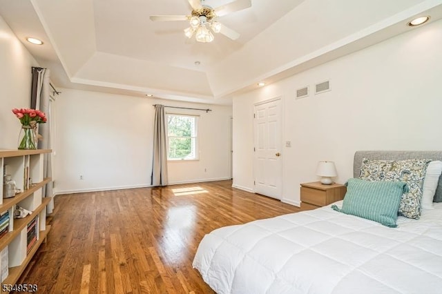 bedroom with a tray ceiling, wood finished floors, recessed lighting, baseboards, and ceiling fan