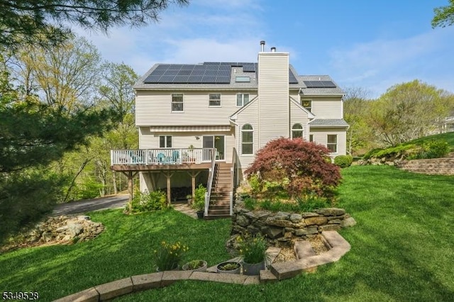 back of house featuring a deck, stairway, a chimney, a yard, and roof mounted solar panels