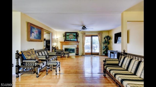 living area featuring a glass covered fireplace, ceiling fan, and wood finished floors