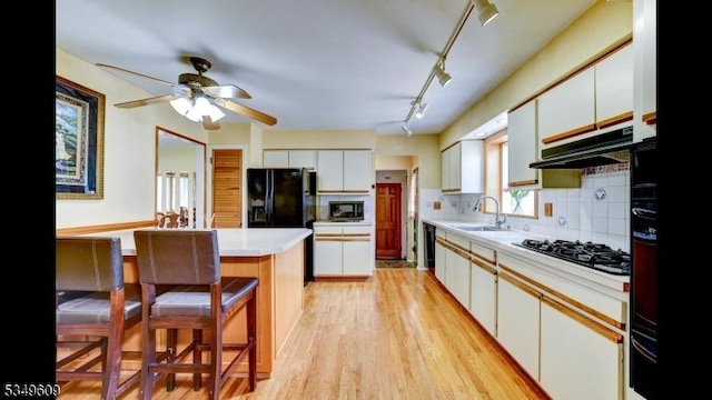kitchen with a breakfast bar, light countertops, under cabinet range hood, a sink, and black appliances