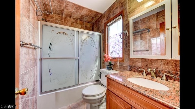 full bathroom featuring tile walls, enclosed tub / shower combo, vanity, and toilet