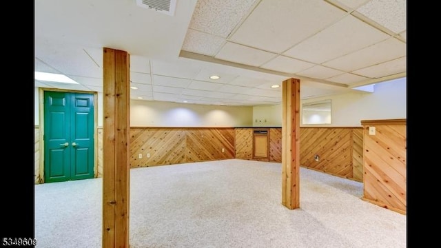 finished basement featuring carpet floors, a drop ceiling, wood walls, and visible vents