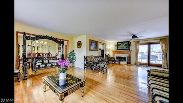 living room featuring a glass covered fireplace, ceiling fan with notable chandelier, and wood finished floors
