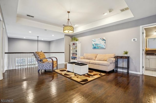 living room featuring a tray ceiling, visible vents, and hardwood / wood-style flooring