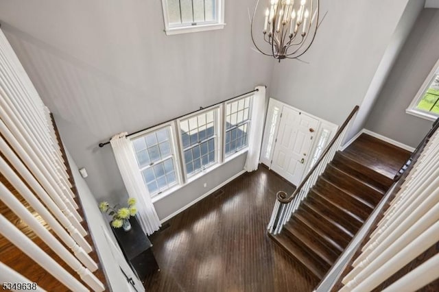 stairs featuring a towering ceiling, baseboards, wood finished floors, and a notable chandelier