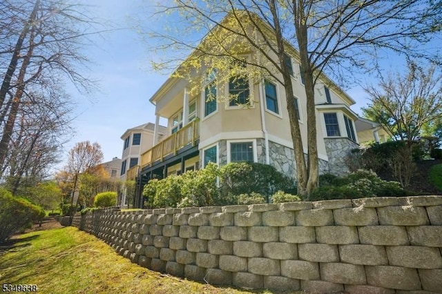 view of side of home featuring stucco siding, a balcony, stone siding, and fence