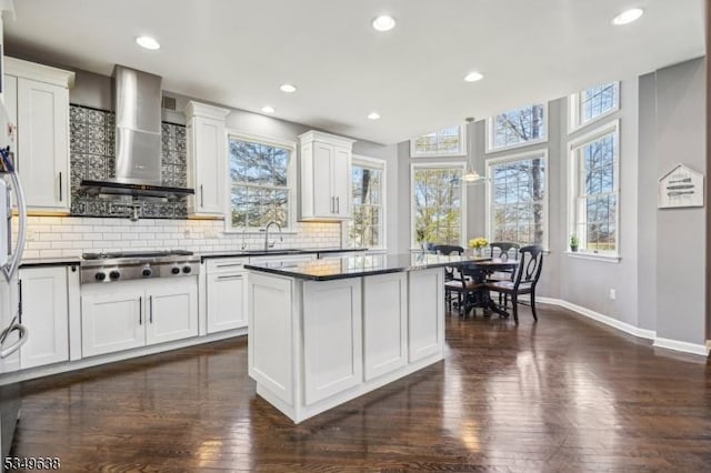 kitchen featuring dark countertops, dark wood finished floors, baseboards, stainless steel gas stovetop, and wall chimney exhaust hood