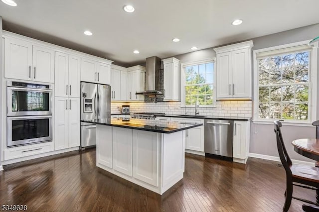 kitchen with dark wood-style flooring, dark countertops, a sink, stainless steel appliances, and wall chimney exhaust hood
