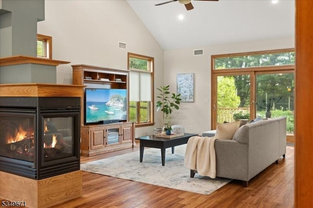 living area with high vaulted ceiling, a ceiling fan, wood finished floors, a multi sided fireplace, and recessed lighting